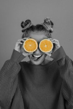 a woman holding two oranges up to her eyes