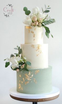 a three tiered cake with white flowers and greenery on the top is sitting on a stand