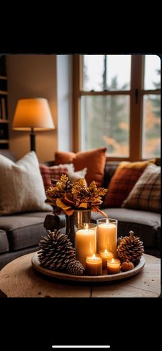 candles and pine cones sit on a tray in front of a couch