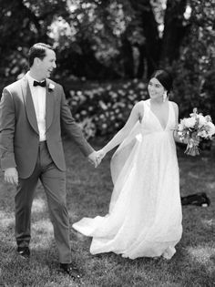 a bride and groom hold hands as they walk through the grass