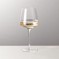 a wine glass filled with white wine on top of a table next to a gray wall