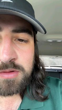 a man with long hair and a beard wearing a hat in the back seat of a car