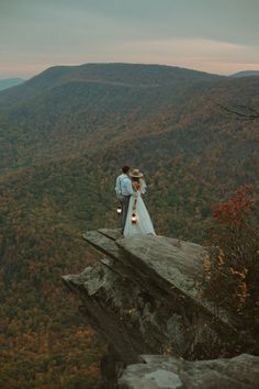 a bride and groom standing on top of a cliff