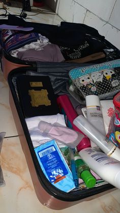 an open suitcase filled with personal items on a counter next to a bottle and toothbrush