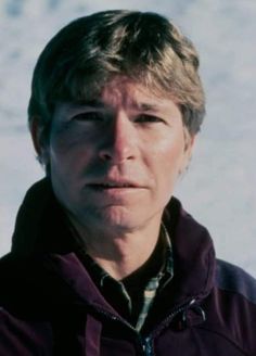 a man standing in front of snow covered ground wearing a purple jacket and looking at the camera