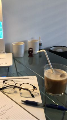 a glass table with glasses, pen and laptop on it next to a cup of coffee