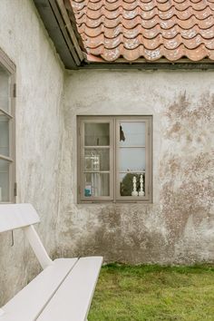 a white bench sitting in front of a window on top of a cement building next to a grass covered field