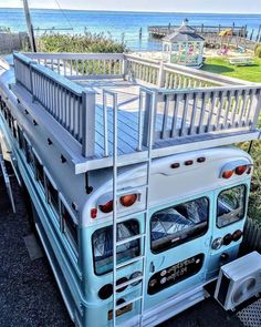 a blue and white bus parked in front of the ocean with a ladder on it's side