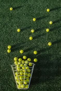 a basket filled with lots of yellow tennis balls on top of a green grass covered field