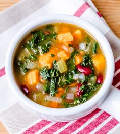 a white bowl filled with vegetable soup on top of a red and white striped towel