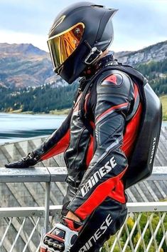 a man wearing a motorcycle suit and helmet leaning on a railing