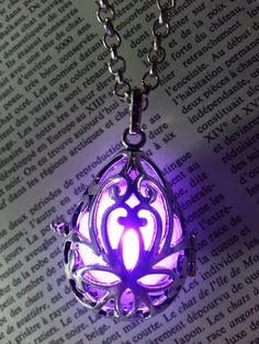 a glowing purple necklace with an intricate design on the front and back side, sitting on top of a book