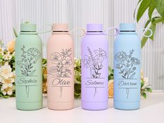 three different colored water bottles sitting next to each other on a white table with flowers in the background