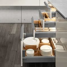 an open drawer in a kitchen filled with plates and bowls on top of wooden flooring