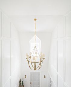 a chandelier hanging from the ceiling in a hallway with white walls and wood floors