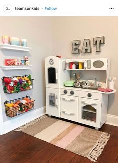 a white play kitchen with lots of food on the shelves and toys in baskets next to it