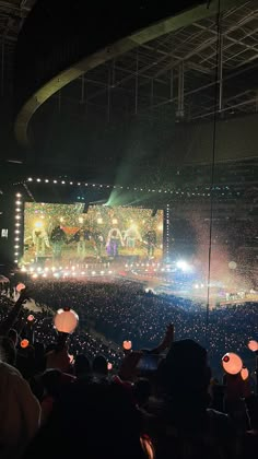 an audience at a concert with balloons floating in the air and lights shining on the stage