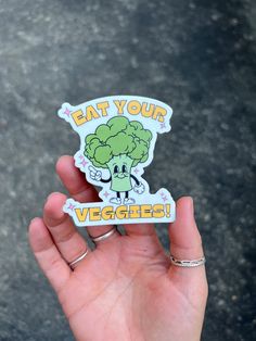 a hand holding a sticker that says eat your veggies