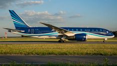 a blue and white airplane is on the runway at an airport with grass in front of it