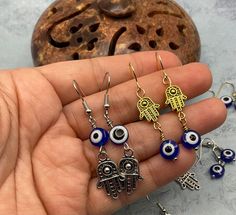 These Evil Eye and Hamsa Hand earrings set are handcrafted personally for me, Derlis. You can choose from 6 different styles on golden or silver tone finish. MATERIALS:   - Dark Blue Evil eye flat round bead, 8mm and 6mm(These resin beads are handmade so it is normal if the eye is a little inconsistent)  - Antique golden Hamsa hand spacer bead, Tibetan Alloy, 12x10mm, double-sided - Antique Silver Hamsa hand charm 20.5x 12.5mm, one-sided - Rhodium and gold finish fishhook earwires All materials Handmade Artisan Blue Earrings, Artisan Handmade Blue Earrings, Blue Round Beads Spiritual Earrings, Blue Spiritual Earrings With Round Beads, Blue Handmade Spiritual Earrings, Handmade Blue Earrings For Gift, Handmade Blue Spiritual Earrings, Handmade Blue Earrings As A Gift, Bohemian Evil Eye Earrings As Gift