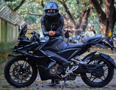 a person wearing a helmet and sitting on a black motorbike in the park