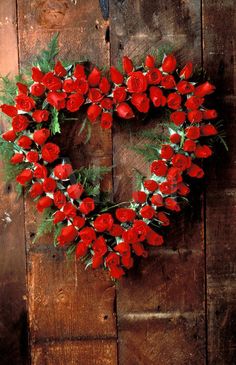 a heart shaped wreath with red flowers on a wooden wall