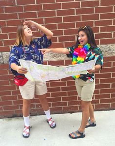 two girls are holding up a map in front of a brick wall and pointing at it