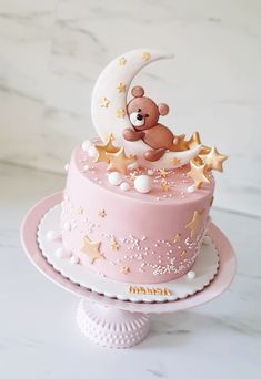 a pink cake with gold stars and a teddy bear sitting on the top of it