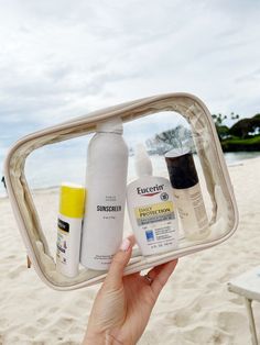 someone is holding up a clear case on the beach with sunscreen and deodorant