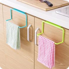 two towels hanging from hooks on the side of a kitchen counter next to a cutting board