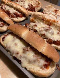 several hot dogs in buns with cheese and meat on them sitting on a baking sheet