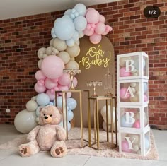 a teddy bear sits in front of a backdrop with balloons and letters for a baby shower