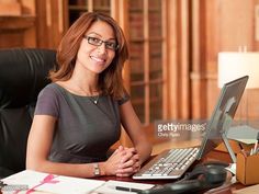 a woman sitting at a desk with a laptop computer in front of her, smiling