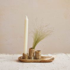 a white candle and two wooden utensils on a tray with some grass in it