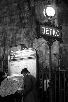 black and white photograph of people waiting at metro station with umbrellas in the rain