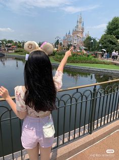 a woman standing next to a metal fence near a pond and castle in the background