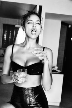 a black and white photo of a woman in a bra top holding a glass with her mouth open