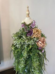 a mannequin with flowers and greenery on it's head is shown in front of a white wall