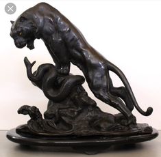 a bronze statue of a cat and a snake on a marble base in front of a white wall