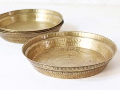 three metal bowls sitting next to each other on a white tableclothed surface with one empty bowl in the middle