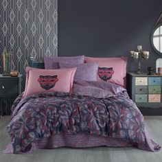 a bed covered in purple and pink comforter next to a dresser with mirror on it