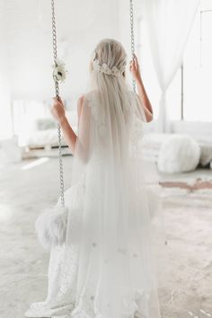 a woman in a white wedding dress is on a swing with her veil pulled back