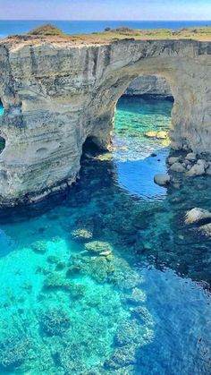 the water is crystal blue and clear at the cliffs near an arch in the cliff