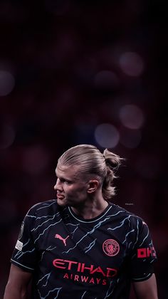 a female soccer player with ponytails in a black uniform looking to the side on a dark background