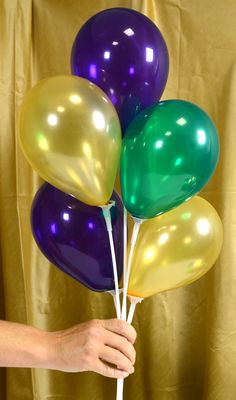 a person holding several balloons in front of a gold curtain with green, purple and yellow colors