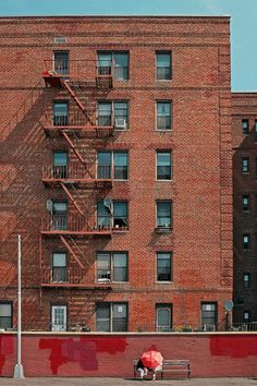 a person sitting on a bench with an umbrella in front of a tall brick building