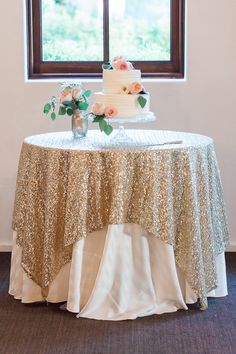 a wedding cake on top of a table with gold sequins and flowers in front of a window