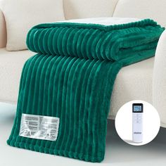 a green blanket sitting on top of a couch next to a white sofa with an electronic thermometer