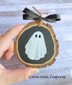 a hand holding a wooden ornament with a ghost painted on it