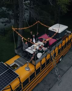 a group of people riding on the back of a yellow bus with lights strung across it